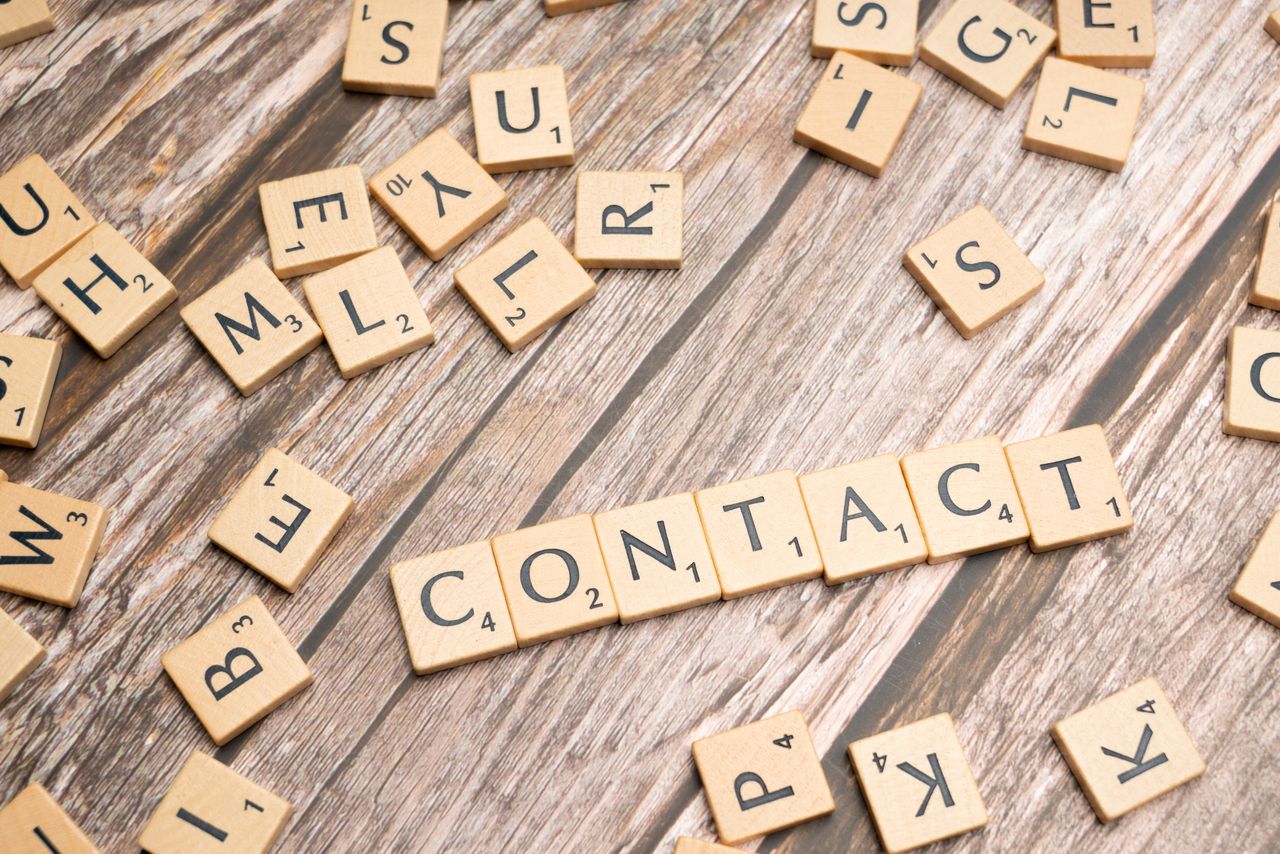 Scrabble-like letter tiles arranged to spell contact on a wooden surface.